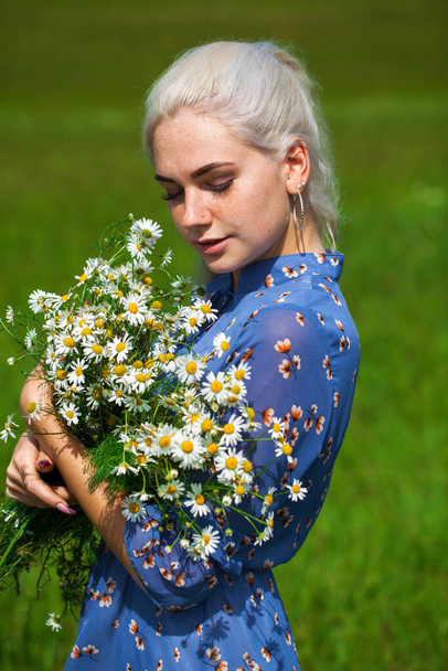 close up portrait of a young blonde girl with a bouquet of chamomile in a field - Foto, afbeelding