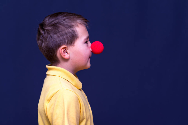 Vista lateral Retrato de niño con camiseta amarilla nariz de payaso, concepto de nariz roja. - Foto, imagen