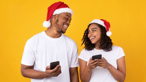 Pár télapó kalap segítségével okostelefonok karácsonyi alkalmazás, sárga háttér - Fotó, kép