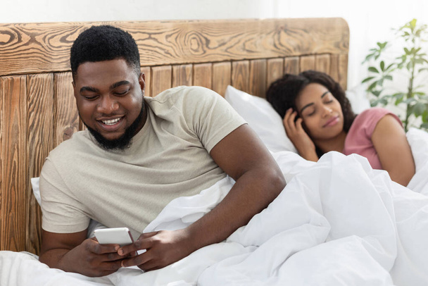 Smiling black man chatting with lover while wife sleeping - Foto, afbeelding