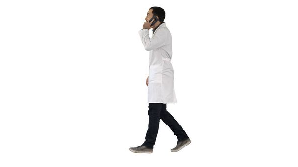 Young doctor talking to mobile and walkind on white background. - Fotografie, Obrázek