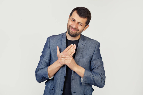 Young businessman man with a beard in a jacket, suffering from pain in the hands and fingers, inflammation of arthritis. Portrait of a man on a gray background. - Fotoğraf, Görsel