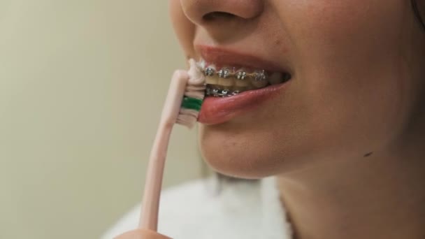 Cerrar mujer limpiando los dientes con aparatos ortopédicos con cepillo de dientes rosa. Limpieza de soportes, higiene dental, autocuidado matutino.  - Metraje, vídeo