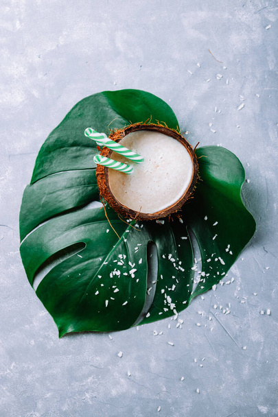 Coconut milk in coconut shell on green monstera leaf. High quality photo - Foto, afbeelding