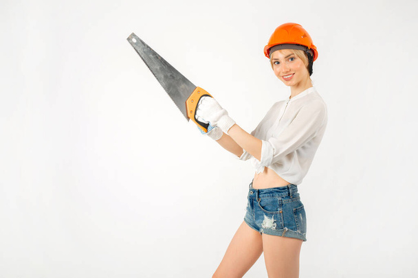 beautiful young female in a construction helmet with a saw in hand - Foto, afbeelding
