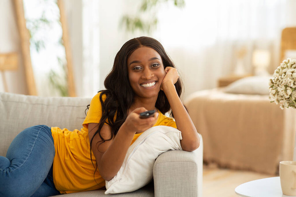 Viikonlopun vapaa-ajan harrastukset. Millennial musta nainen kaukosäädin kytkentä kanavat televisiossa kotona, kopioi tilaa - Valokuva, kuva