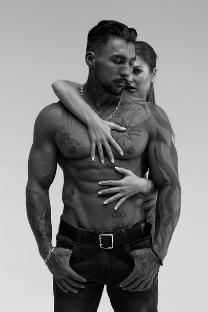 Black and white side view of topless woman and shirtless man looking at camera against gray background - Foto, Imagem