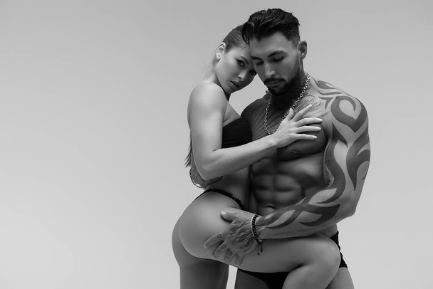 Hombre sin camisa tatuado blanco y negro y mujer en topless seductora mirando hacia otro lado - Foto, Imagen
