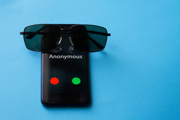 Un smartphone avec un appel anonyme se trouve sur une surface bleue à côté des lunettes de soleil. Le problème de l'anonymat et de l'espionnage. Protection des renseignements personnels. Espace de copie gratuit - Photo, image