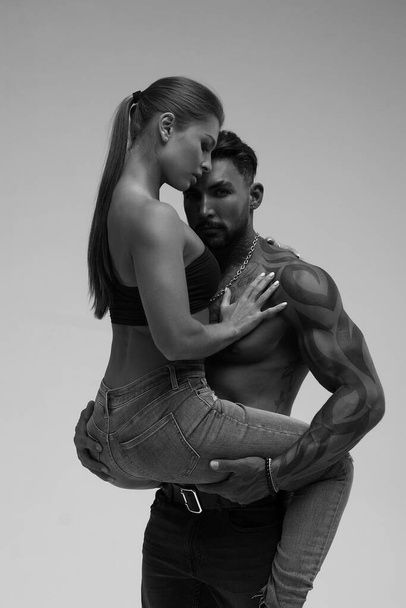 Черно-белые татуированные мужчина без рубашки и соблазнительная топлесс женщина смотрит в сторону - Фото, изображение