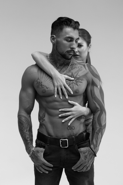 Black and white side view of topless woman and shirtless man looking at camera against gray background - Фото, изображение