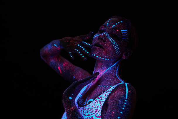 Művésznő kozmosz ultraibolya fényben. Az egész testet színes cseppek borítják. Egy lány pózol a sötétben. Zaj, nem fókuszált - Fotó, kép