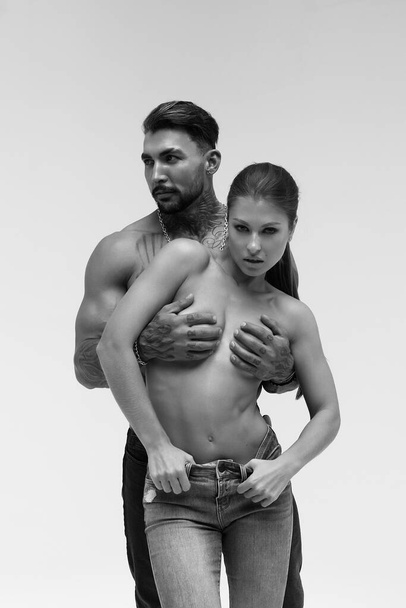 Black and white side view of topless woman and shirtless man looking at camera against gray background - Foto, Imagem
