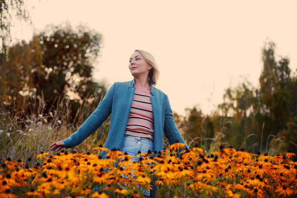 Blondynka biała kobieta z fryzurą Boba wirująca na jesiennym polu wśród pomarańczowych kwiatów z rozłożonymi dłońmi. Koncepcja wolności i szczęścia. Uśmiechnięta kobieta na zewnątrz portret - Zdjęcie, obraz