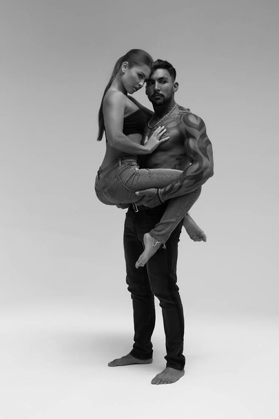 Black and white side view of topless woman and shirtless man looking at camera against gray background - Photo, Image