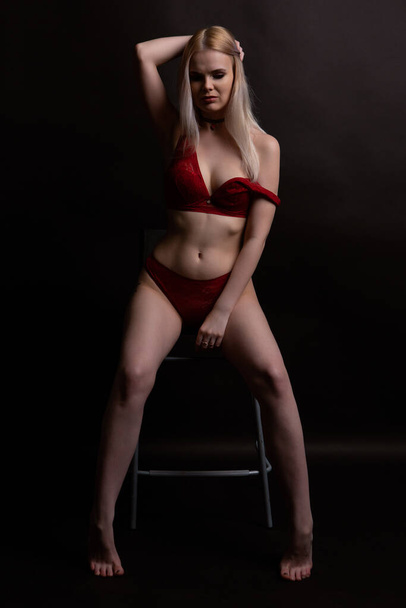 Sexy blonde woman in Lacy red underwear erotic sitting on a chair looking at the camera - Фото, изображение