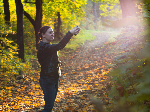 a young woman in a leather jacket in a Park takes a selfie. autumn in the Park - Foto, imagen