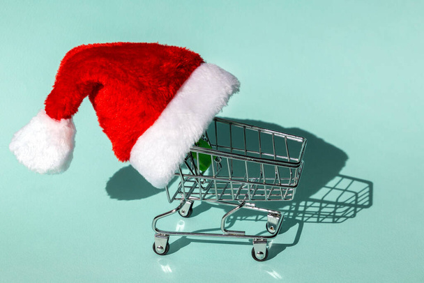 Shopping cart in a santa hat. Christmas and New Year shopping sale concept - Foto, afbeelding