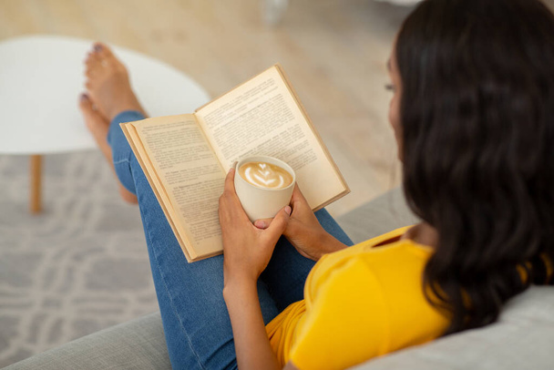 Donna afroamericana che si prende una mattinata pigra con cappuccino aromatico e libro accattivante a casa - Foto, immagini