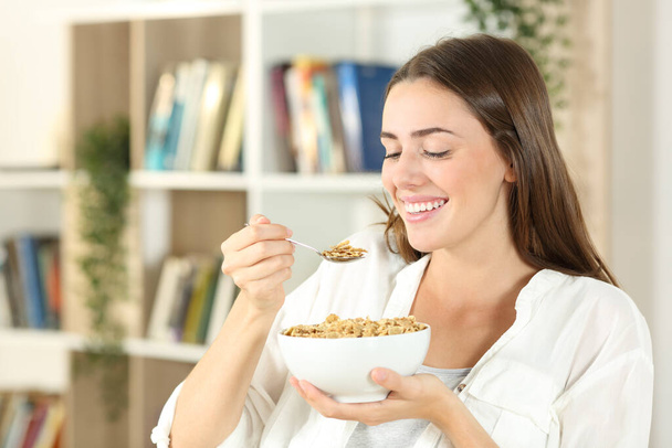 Happy woman eating cereals for breakfast sitting at home - Zdjęcie, obraz