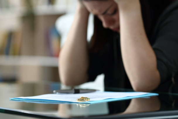 Sad wife complaining after signing divorce document with wedding rings over it at home - Photo, Image