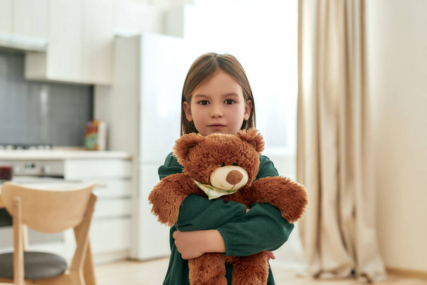 A small cute girl tightly holds her fluffy toy while looking into a camera - Foto, immagini