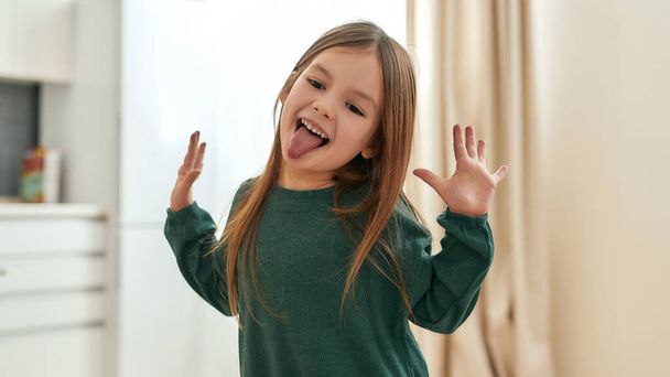 A small happy girl playing around emotionally smiling with her tongue out and her hands raised with palms open - Foto, imagen