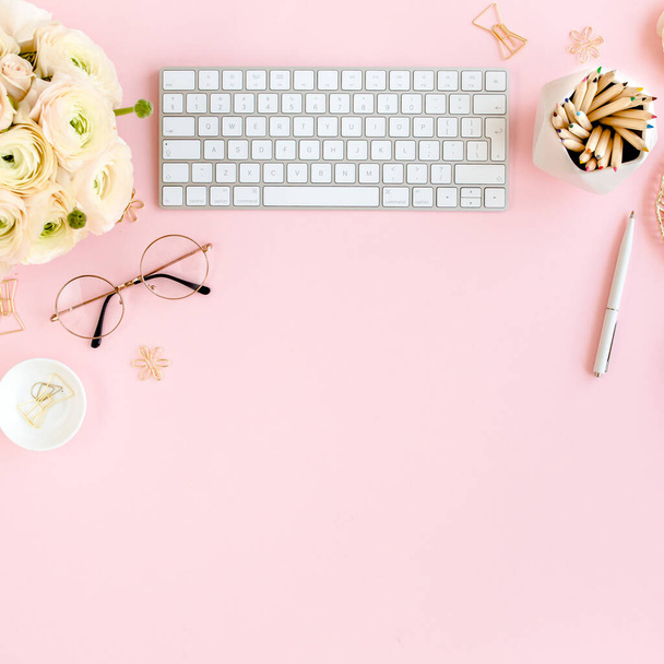 Stylized, pink womens home office desk. Workspace with computer, bouquet ranunculus and roses, clipboard on pink background. Flat lay. Top view. - 写真・画像