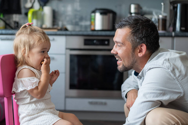 A cute little girl and her dad are eating in the kitchen - Zdjęcie, obraz
