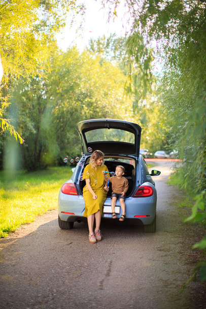 Beautiful mother and little son travelers sit in trunk of car on road and blow soap bubbles. Photo about family travel - Photo, Image