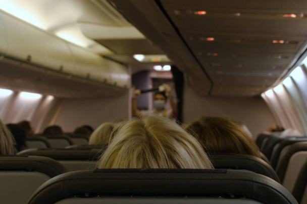 head of blonde woman rear view in cabin of plane on blurred background of stewardess giving briefing before departure - Photo, Image
