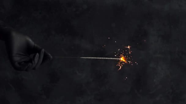 Egy kéz egy fekete orvosi kesztyűben egy égő csillagszórót tart. függőleges látószög - Felvétel, videó