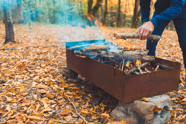 Picnic. A man throws logs on the grill. Autumn forest in the background. Close up. - Photo, Image