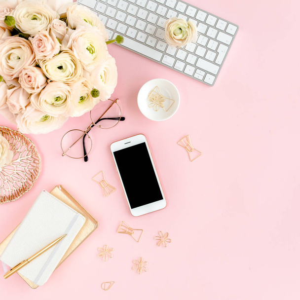 Stylized, pink womens home office desk. Workspace with computer, bouquet ranunculus and roses, phone on pink background. Flat lay. Top view. - 写真・画像