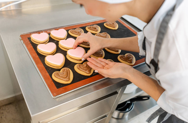 Кондитерська жінка використовує мішок для випічки, щоб покласти вершки на печиво
 - Фото, зображення