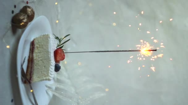 Festliches weißes Kuchenstück mit brennender Wunderkerze auf hellem Hintergrund. vertikale Bildschirmorientierung. - Filmmaterial, Video