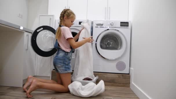 Figlia adolescente che fa i lavori domestici in lavanderia e mette il bucato sporco in lavatrice. Ragazza che aiuta sua madre. Rallentatore - Filmati, video