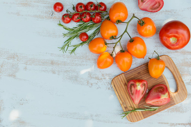 Various colorful tomatoes and rosemary herb on light blue background - 写真・画像