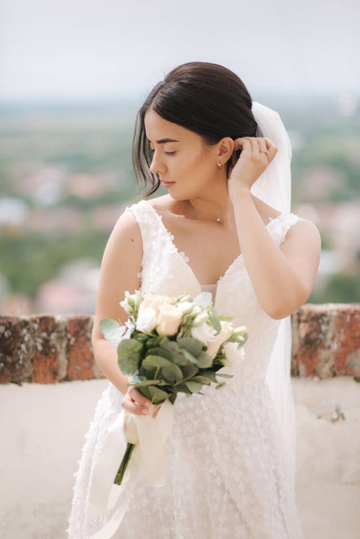 Beautiful bride stand in frind of city view with bouquet and smile - Fotografie, Obrázek