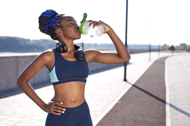 black gorgeous woman fitness instructor drinking water during the training exercises outdoors - Фото, изображение