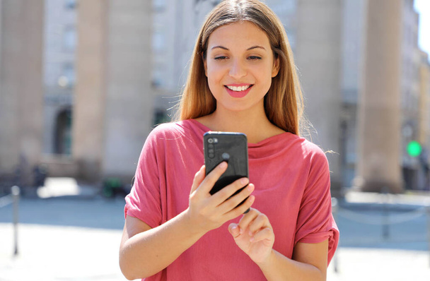 Prachtige mooie jonge vrouw met lang haar chatten op de smartphone in de stad straat. mooi meisje het hebben van smart phone gesprek outdoor. - Foto, afbeelding