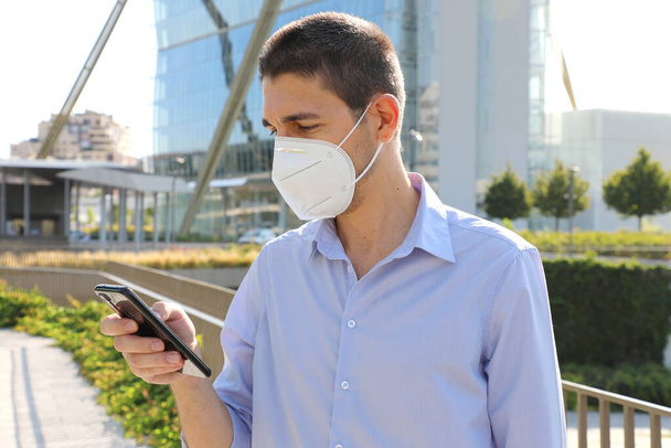 Homme d'affaires avec masque de protection KN95 appelant avec smartphone dans la ville moderne - Photo, image