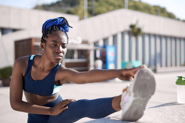 black woman runner stretching leg muscle before running outdoors - Foto, imagen
