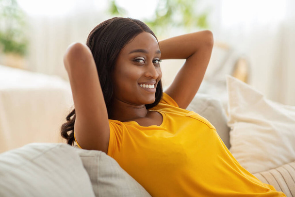 Peaceful weekend morning at home. Beautiful black lady relaxing on comfortable couch indoors - Photo, image