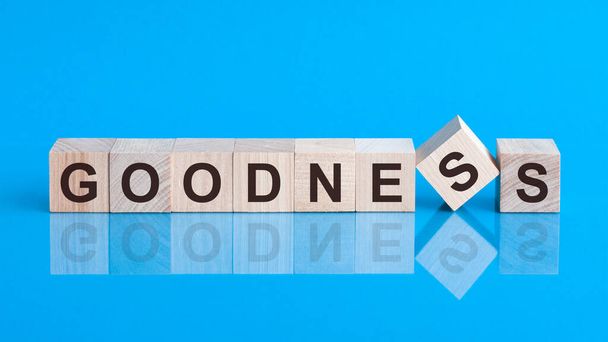 Text goodness on wood cube block, stock investment concept. The text goodness is written on the cubes in black letters, the cubes are located on a blue glass surface. - Photo, image