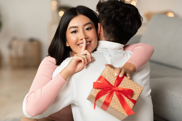 Coreano fidanzata abbracciare fidanzato holding regalo dietro la schiena all'interno - Foto, immagini