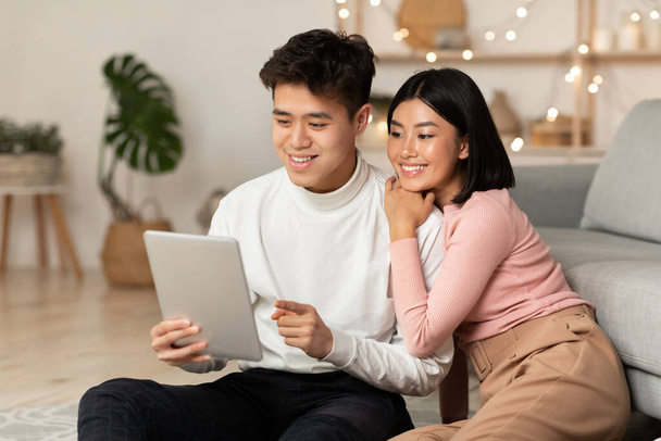 Ευτυχισμένο ζευγάρι Κορέας χρησιμοποιώντας Tablet υπολογιστή κάθεται στο σπίτι - Φωτογραφία, εικόνα