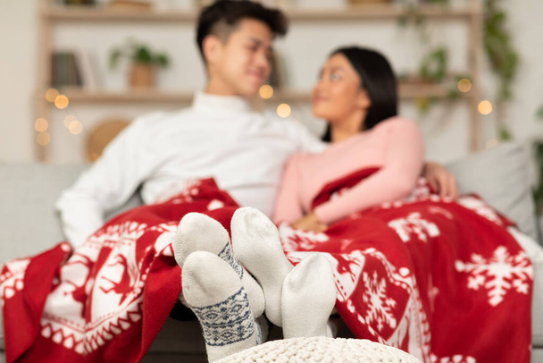 Asiatisches Paar sitzt bedeckt mit Decke und feiert Weihnachten zu Hause - Foto, Bild