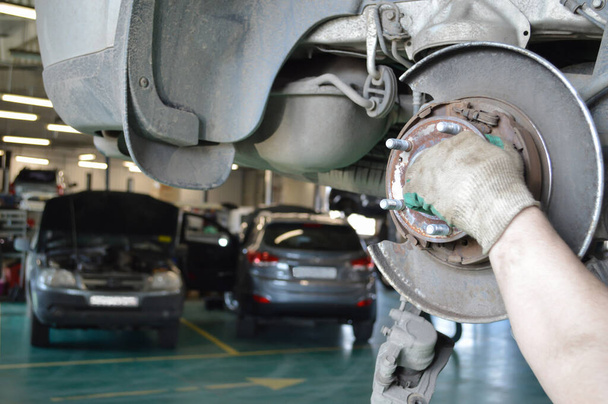 Un mécanicien de voiture dans des gants de travail enlève le moyeu arrière d'une voiture dans un atelier de réparation automobile - Photo, image