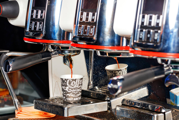Во время приготовления ароматного кофе кофеварка наливает кофе в картонную чашку. - Фото, изображение